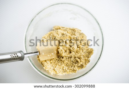 Fresh mixed lemon and poppy seed biscuit dough in glass mixing bowl with spatula, overhead shot.