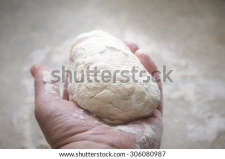 Hand holding a ball of homemade bread or pizza dough, ready for kneading.