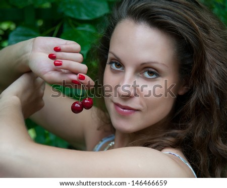 sensual woman eating a cherry on a background of foliage