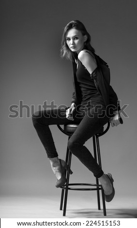 stylish adult girl in a jacket sits on a chair on a gray background