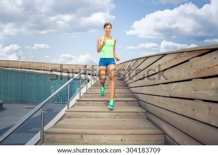 sportswoman running on wooden stairs under blue cloudy sky