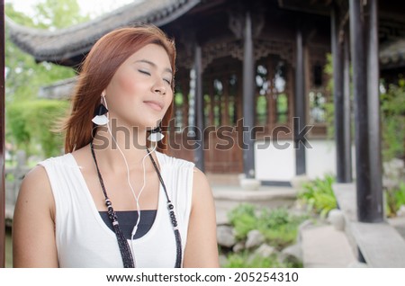 Closed-eyes young woman enjoying her music sitting in the garden wearing ear plugs listening to tunes on her music player