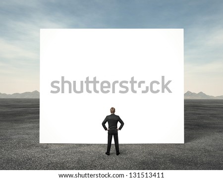 Businessman looking at white empty billboard in the desert
