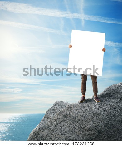 Man standing on a rock with blank poster in his hands