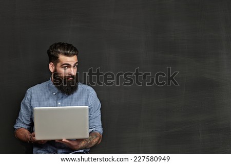 Bearded man with laptop standing near chalkboard
