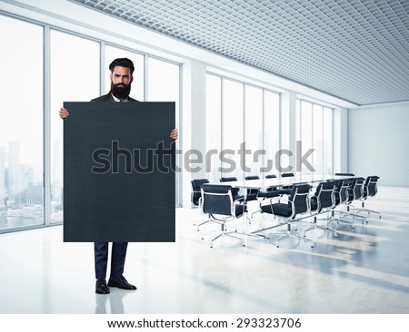 Bearded businessman holding blackboard at contemporary office