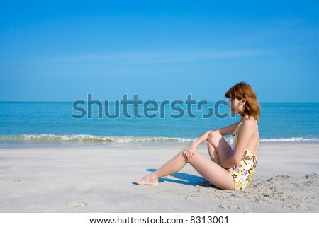 woman wearing floral swimsuit sit by the beach looking forward smiling and relaxing