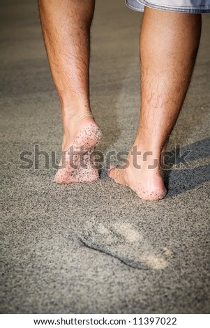 legs of a man walking leaving foot print on the sandy beach