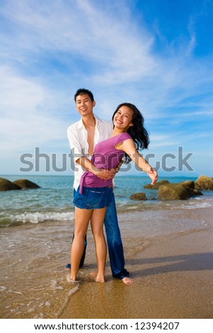 loving couple hugging each other on the beach during summer time with bright blue sky