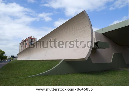 Wide angle shot of an architectural detail looking like half of a half-pipe. Blue sky and a couple of buildings in the background. Copy space in perspective.