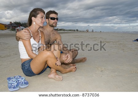Young healthy couple sited in the sand, looking out into the sea (side shot).