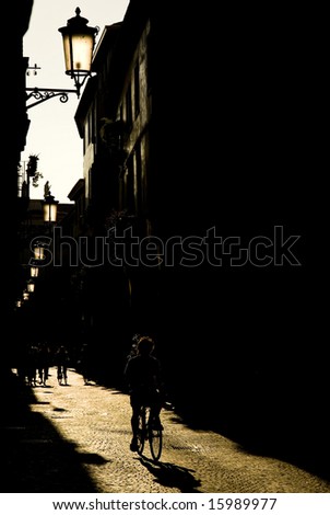 Sepia toned old street in Padova, Italy, with silhouette of cyclist and backlit old lightpost