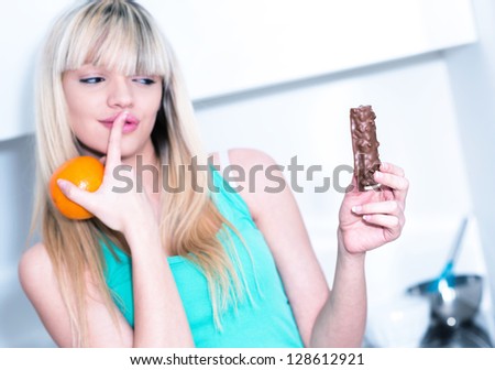 woman hesitating between a candy bar and an orange