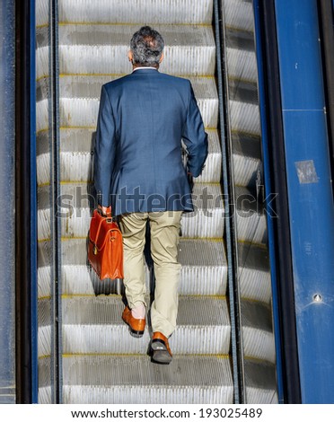 Back view of business man taking the escalator to get to work
