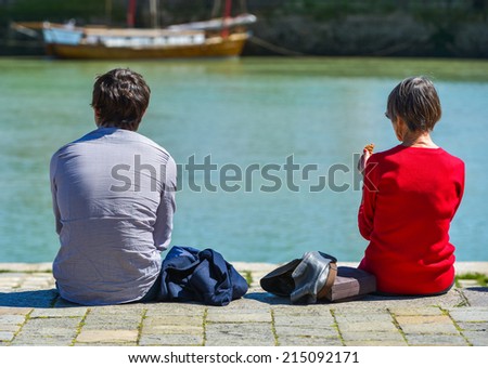 A man and a woman sitting at the pier and looking at the sea with the blury view of a ship in the background