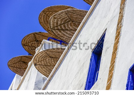 Low-angle shot of large straw umbrellas on different floors of the white building with blue windows