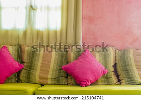 Bright colorful cushions on the sofa with light coming in from the curtain-covered window on the background