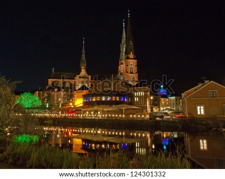 A scenic view of the west side of Fyris river by night with Uppsala Cathedral behind a market hall with its popular restaurants. Uppsala, Sweden