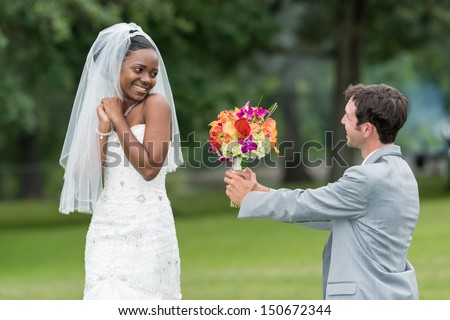 Groom kneeling down to hand flower to bride