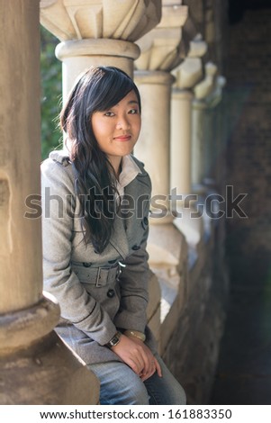 Young woman sitting next to a row of stone pillars
