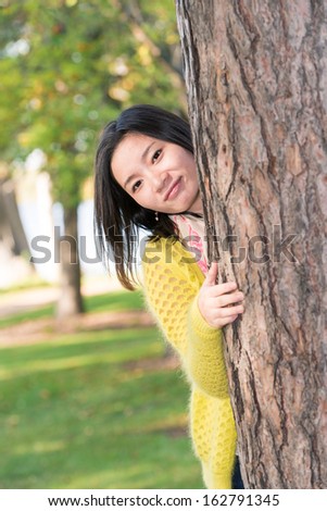 portrait of shy young woman peaking from behind a tree and smiling