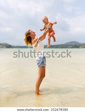 Happy family. Young mother throws up her baby in the sky on a sunny day. Photo of a mother and her little son playing on the beach. Positive human feelings and emotions.