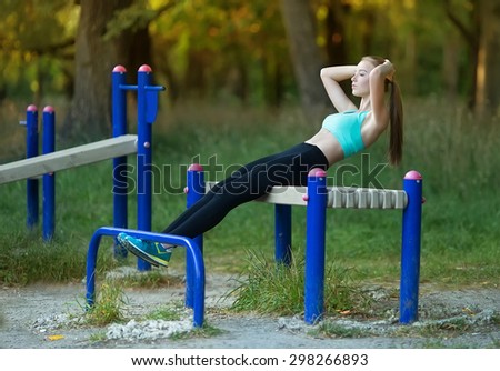 Warming-up. Beautiful young caucasian woman in fitness wear doing belly press exercises in a park at the morning