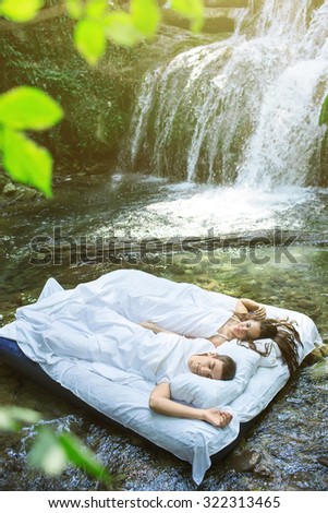 A hidden place. Sleeping couple in deep forest lies on airbed. Waterfall on back