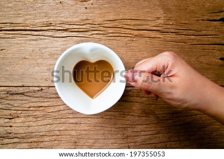 Hand Holding Drinking, Coffee Mug in Design of Heart Shape, Love and Romantic or Valentine\'s Concept and idea on Wood Table Background, Rustic Style.
