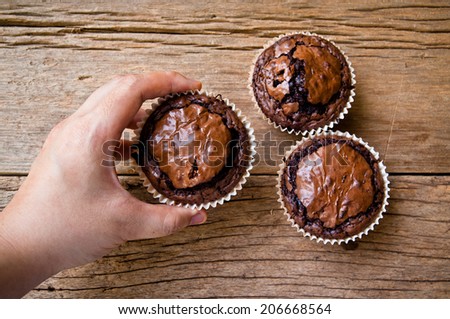 Hand, Chocolate muffins with crispy top on Wood Table Background, Rustic Still Life Style / Concept and Idea of Sweet Food Bakery Dessert Time, To Eat with Coffee or Hot Drink in Morning or Tea Time.
