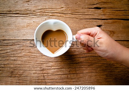 Hand Holding Drinking Coffee Mug in Design of Heart Shape, Love and Romantic or Valentine\'s Day Concept and idea of Love Sweet Sharing on Wood Table Background, Rustic Still life Style.