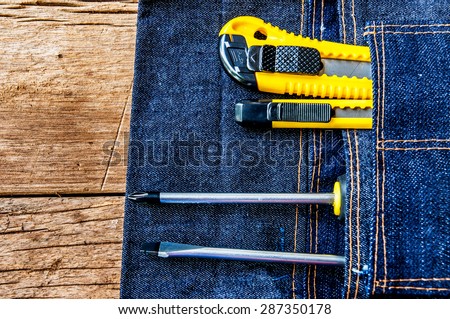Metal Screw Driver with Stationery Knife Cutter Work Tools in Denim Tool Bag on Wood Table background / Concept and Idea of Industrial, Handmade, Home Improvement, Worker, Business or Art Crafts.