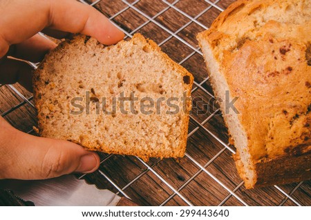 Banana Bread Loaf, Fresh Baked from Oven Sliced with Knife, Hand Holding on Cooking Rack and Wood Background, Vintage Country Rustic Still Life Style. Concept and Idea of Breakfast, Bakery.