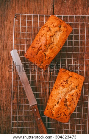 Banana Bread Loaf, Homemade Fresh Baked from Oven with Knife, on Cooking Rack and Wood Background, Vintage Country Rustic Still Life Style. Concept and Idea of Breakfast, Bakery. Top View Vertical.