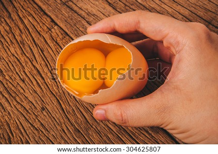 Double Yolks, Fresh Twin Egg Yolks in Egg Shell with Hand Holding on Wood Table Background, Country Rustic Style. Concept Idea of Cooking and Baking.
