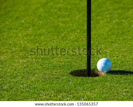 Rolling Golf Ball falling into Cup with a Black Flag Stick on a Green.