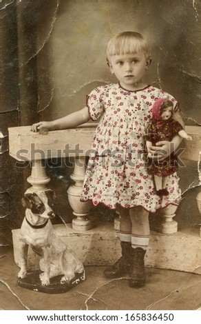 WARSAW, POLAND, CIRCA TWENTIES - Manually colored vintage photo of little girl with a doll and dog statue, Warsaw, Poland, circa twenties