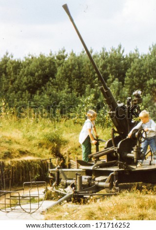 Vintage photo (scanned reversal film) of brother and sister playing in open air military museum (early eighties)