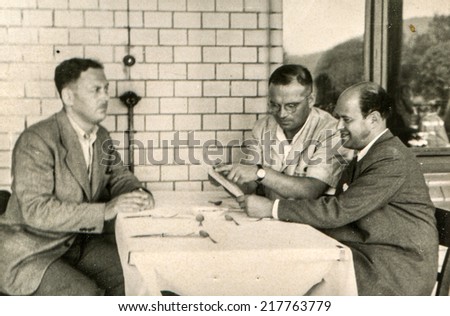 LODZ, POLAND, CIRCA FIFTIES - Vintage photo of three man studying menu in restaurant