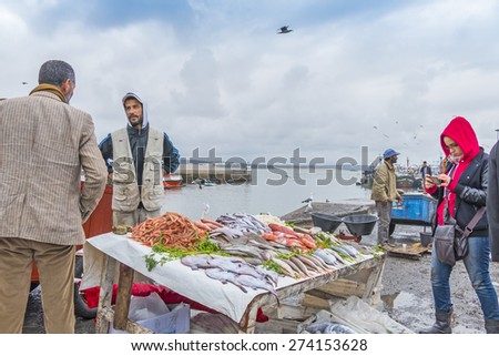 AS-SAWIRA, MOROCCO, APRIL 7, 2015:  Fishermen sell fish and seafood in port of As-Sawira while a tourist takes photos with her cellphone