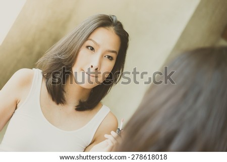 Young asian woman make up yourself looking mirror - vintage soft effect and light filter processing