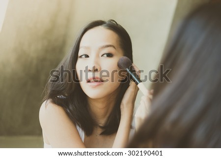 Young asian woman make up yourself looking mirror - vintage soft effect and light filter processing