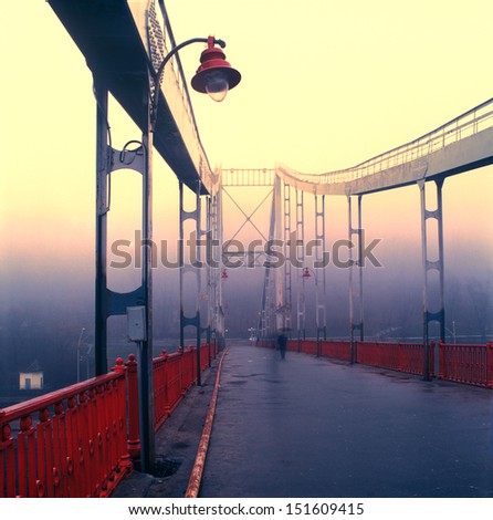 Old pedestrian bridge in Kiev in the early morning mist, the lone passer goes to work
