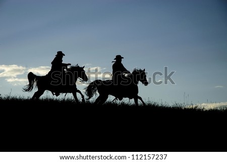 Two cowboys silhouetted against a Montana dawn sky