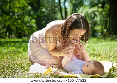 Young mother kissing feet of her baby lying on back - sunny summer day