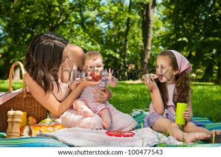 Mother with her two children having picnic in park - showing apple to baby
