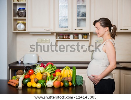 Pregnant woman with abundance of vegetables and fruits in kitchen