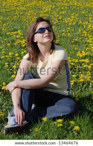 Woman in sunglasses sitting in field of dandelions with face turned to sun