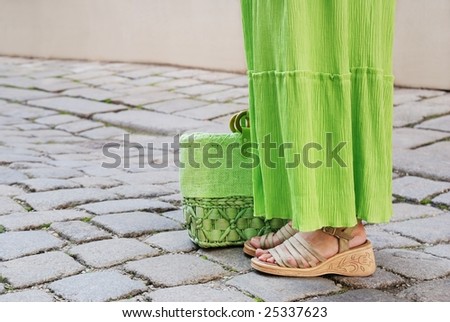 Detail of lower part of young woman in green skirt standing on paving road