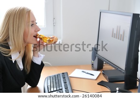 Young business woman siting at work table and eating pizza